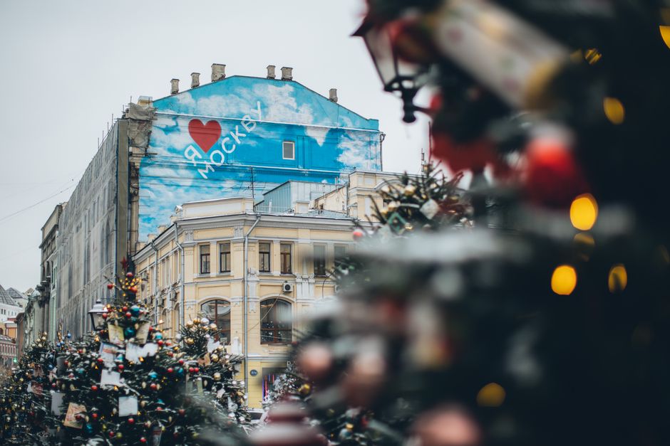 Facade of old building with creative graffiti with inscription located on city square with Christmas trees decorated with ornaments and colorful baubles