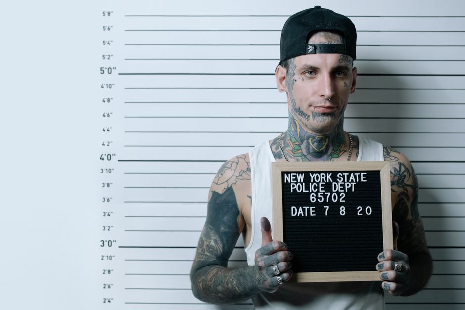 A tattooed man in a white tank top holding a police department sign.