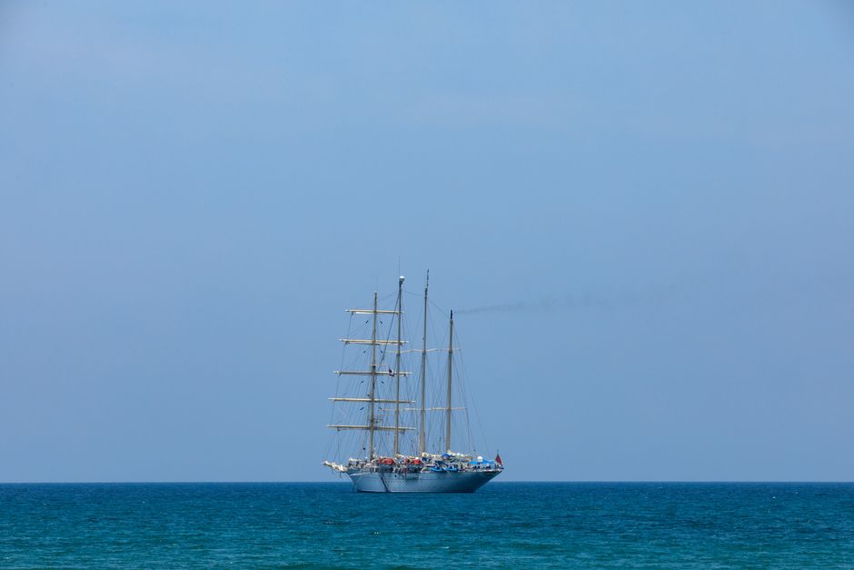 A tall schooner under sail on a clear blue ocean with a vivid sky and masts visible.