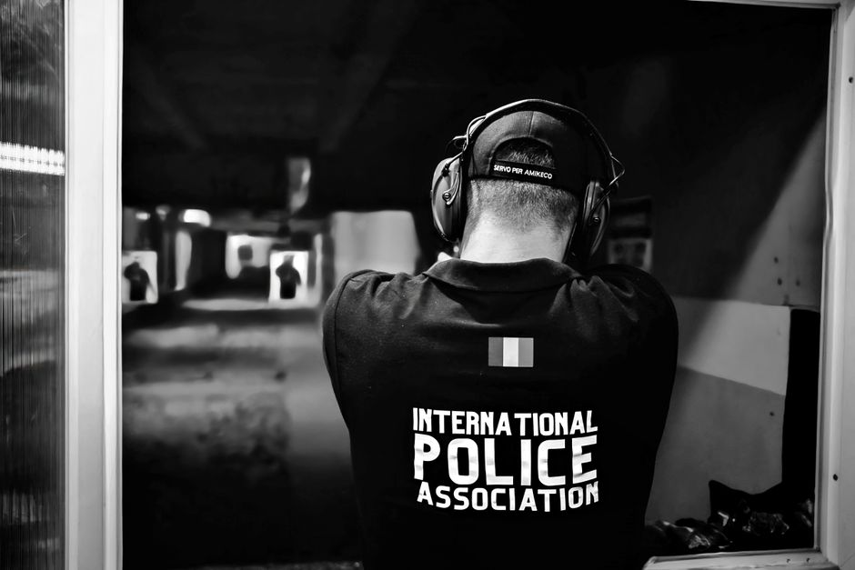 A police officer aiming at targets in an indoor shooting range, shot from behind in black and white.