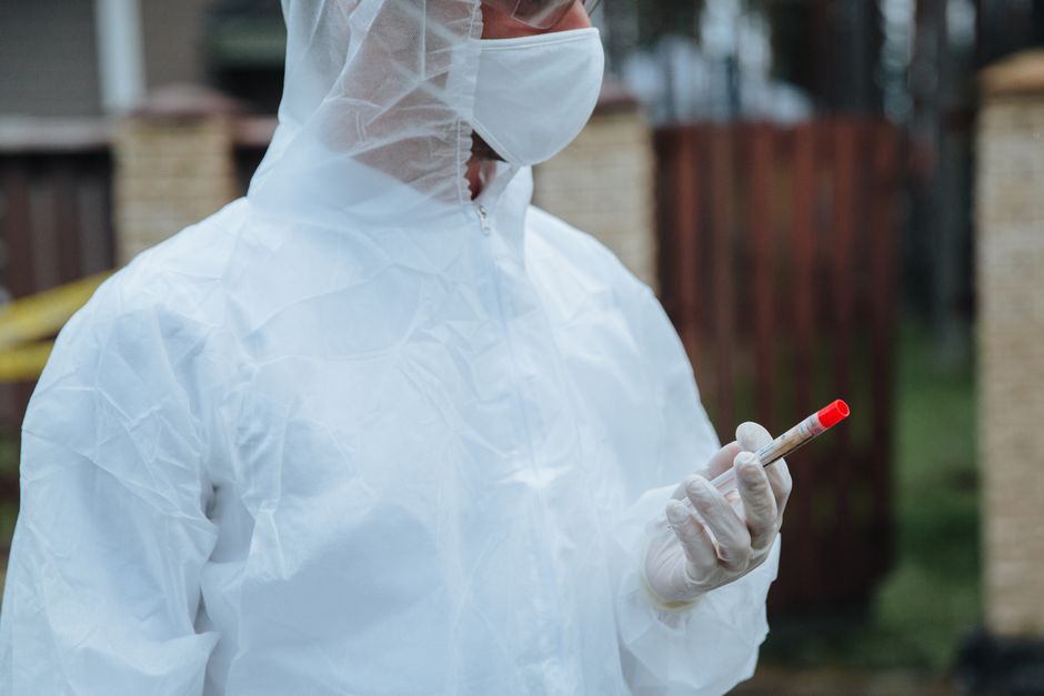 Healthcare professional in protective gear holding a test sample outdoors.