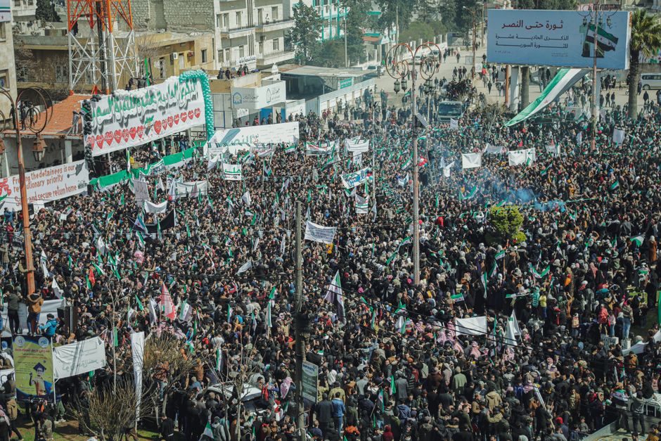 Aerial view of a massive protest in Syria with banners and flags.