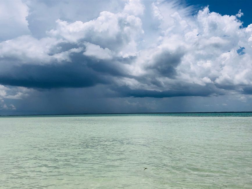 Dramatic storm clouds gather over the turquoise Caribbean Sea near an island.