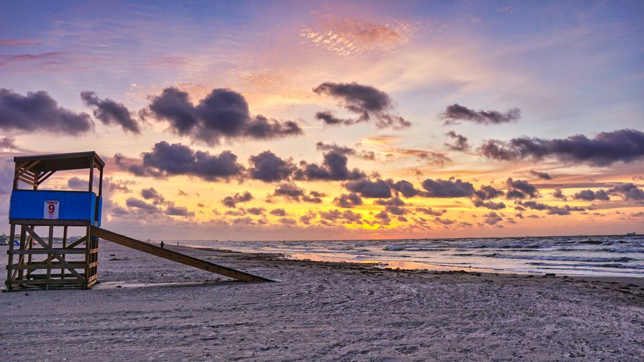 Dramatic sunrise at Port Aransas, TX with lifeguard post and vibrant clouds over the ocean.