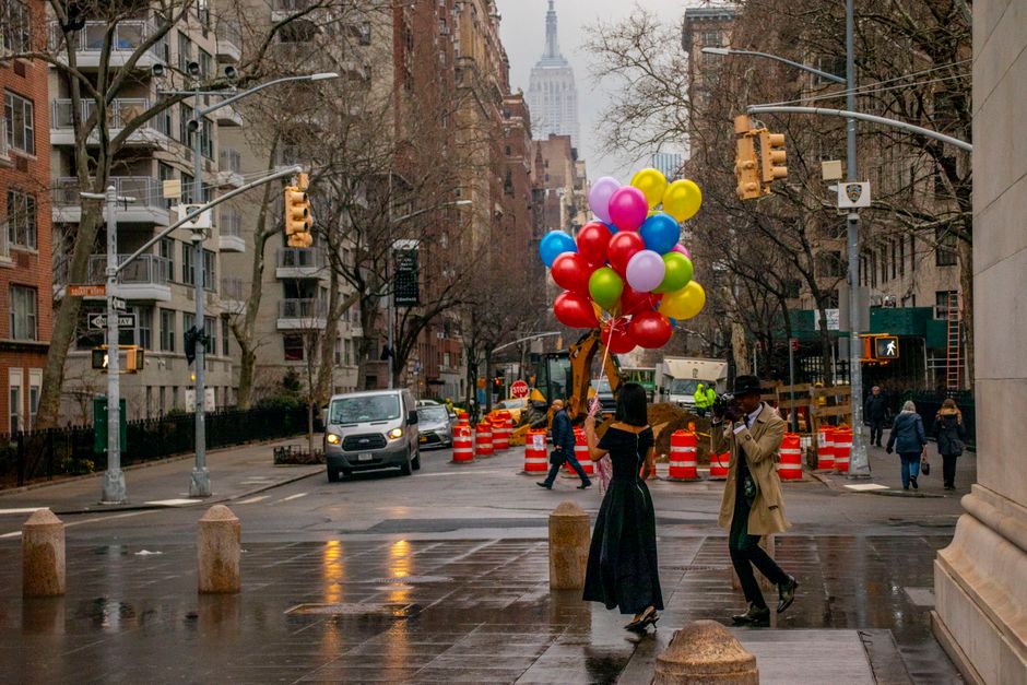 A couple holding balloons on a rainy New York City street with the Empire State Building in the background.