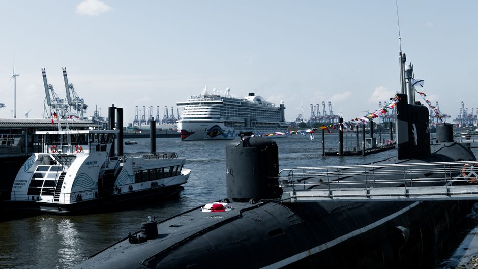 Cruise ship and submarine docked at vibrant Hamburg harbor on a clear day.