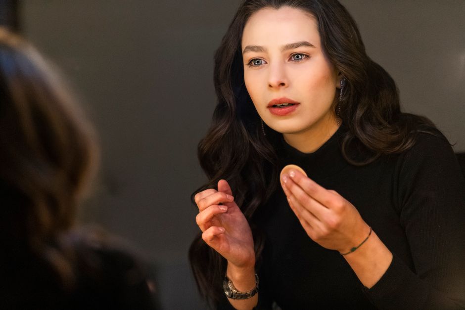 Portrait of a woman applying her makeup in front of a mirror, highlighting her focused expression and style.